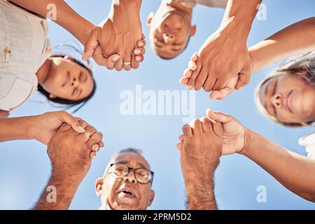 Adoration, prière et famille tenant les mains priant ensemble pour plus de puissance, grâce ou aide spirituelle vue de dessous. Ciel bleu, religion chrétienne personnes a Banque D'Images