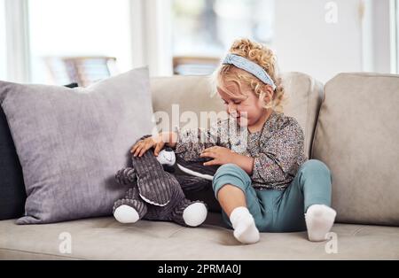 Vous allez vous asseoir là-bas. Photo en longueur d'une adorable petite fille assise seule sur le canapé et jouant avec ses jouets à la maison Banque D'Images