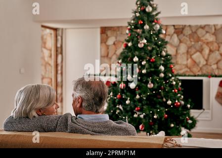 Maintenant étaient officiellement prêts pour Noël. Vue arrière d'un couple adulte méconnu assis ensemble sur un canapé se tenant l'un contre l'autre tout en regardant un Banque D'Images