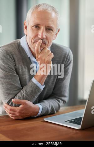 Laissez-moi y réfléchir... Portrait d'un homme d'affaires mûr qui a l'air réfléchi lorsqu'il travaille sur son ordinateur portable au bureau. Banque D'Images