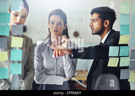 C'est un point intéressant... un groupe de gens d'affaires braque sur un mur de verre avec des notes adhésives dans un bureau. Banque D'Images