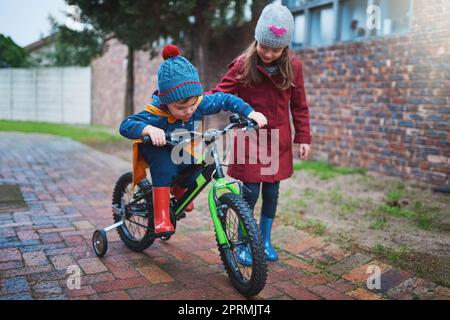 Une grosse sis sera toujours là pour l'aider. Une petite fille qui enseignera à son frère comment faire un vélo dehors. Banque D'Images