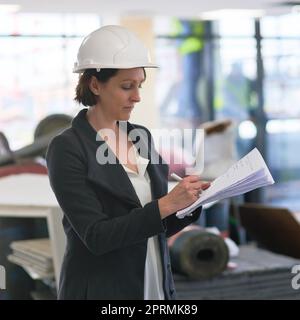 Elle ne manque jamais rien lorsqu'elle fait une liste. Une femme responsable de construction sur place portant un casque. Banque D'Images