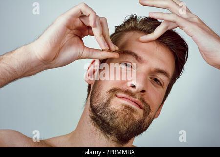 Soyez le patron de vos sourcils. Studio photo d'un beau jeune homme qui pette ses sourcils sur un fond gris. Banque D'Images