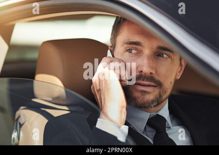 Gestion de l'entreprise en déplacement. Un homme d'affaires utilisant son téléphone tout en conduisant une voiture. Banque D'Images