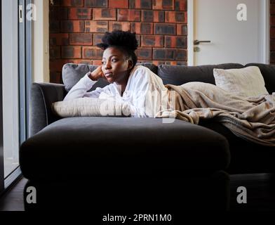 Ennuyé, dépression et isolement avec une femme noire couché sur son canapé pendant un confinement, une quarantaine ou une pandémie. La santé mentale, l'anxiété et le stress chez les jeunes femmes qui pensent et regardent sa fenêtre Banque D'Images