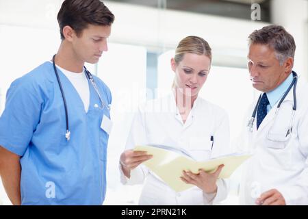 J'ai besoin de conseils pour ce patient... trois professionnels de la santé qui se dansent sur un dossier ensemble à l'hôpital. Banque D'Images