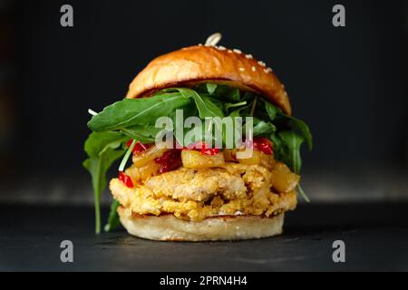 Photo en gros si chickenburger sur fond noir avec fromage, bacon, tomates, salade verte et de chili. Banque D'Images