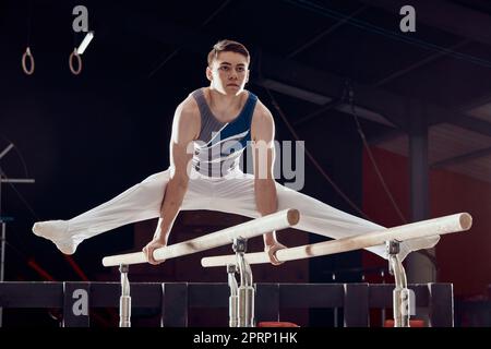 Gym, homme et entraînement pour l'équilibre et la forme physique en gymnastique professionnelle pour les exercices cardio-sportifs la nuit. Jeune homme sportif dans l'exercice de compétition d'acrobat sombre dans la pratique de sport pour la compétition. Banque D'Images