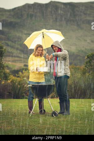 Ensemble, nous pouvons vaincre ce temps. Un couple joyeux qui s'aboie sous la pluie tout en tenant un parapluie et en riant tout le chemin. Banque D'Images