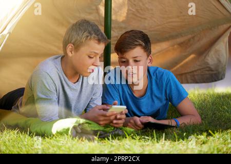 Découvrez-le, dude. Un jeune garçon montrant quelque chose à son ami sur un téléphone portable tout en camping. Banque D'Images