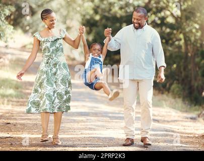 Des parents heureux balancent la fille à leurs mains dans la forêt pendant une promenade dans la nature. Gamin joyeux s'amuser tout en se liant avec la mère et le père lors de vacances d'été en famille ou en faisant des sorties ensemble dans les bois Banque D'Images