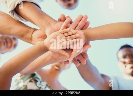 Maintien, amour et mains de famille empilées dans la célébration et l'accord ensemble à l'extérieur sur fond bleu ciel. En dessous de la vue des parents et des enfants montrent l'unité, la foi et la confiance à l'extérieur dans la nature Banque D'Images