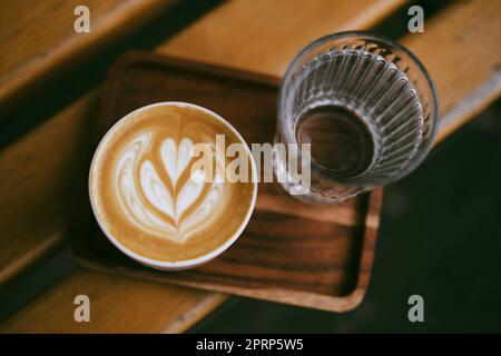 Cappuccino chaud dans une tasse sur un plateau en bois à côté d'un verre d'eau claire Banque D'Images