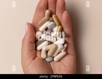 Main avec mélange de capsules médicales sur la vue de dessus beige clair. Prise de compléments alimentaires Banque D'Images