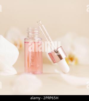 Bouteille de Dropper ouverte près des fleurs d'orchidées blanches sur le beige clair gros plan. Produit de beauté pour les soins de la peau Banque D'Images