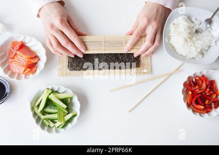 Processus de préparation de sushi, la jeune fille fait des sushis avec différentes saveurs - saumon frais, caviar, avocat, concombre, gingembre, riz. Banque D'Images