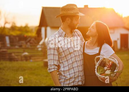 Portrait de jeunes agriculteurs heureux couple tenant le panier avec des légumes frais biologiques sur leur rancho au coucher du soleil. Des aliments sains végétariens. Famille Banque D'Images