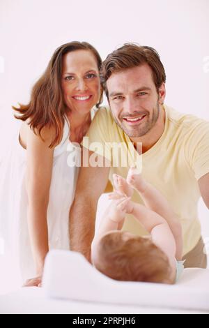 Parents dévoués de la petite fille la plus adorable. Portrait de deux parents amoureux debout sur leur fille bébé alors qu'elle se trouve sur une table à langer. Banque D'Images