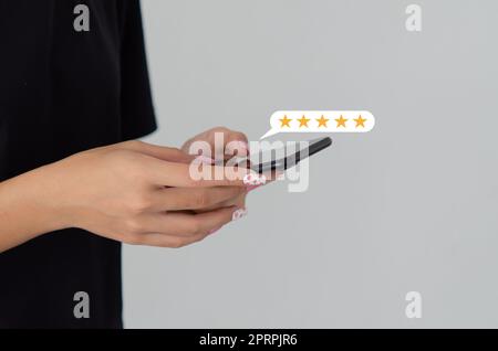 Femme main à l'aide d'un smartphone mobile avec icône cinq étoiles expérience du service client avis satisfaction. Banque D'Images