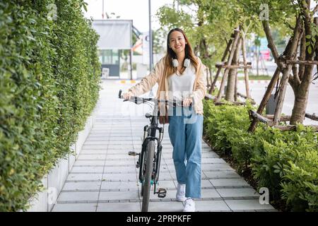 Une femme souriante se promette dans la rue avec son vélo sur la route de la ville Banque D'Images