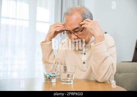 Asiatique homme âgé malade ont mal de tête regardant le verre de pilule sur à la maison Banque D'Images