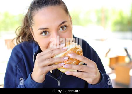 Femme mangeant un hamburger regardant l'appareil photo Banque D'Images