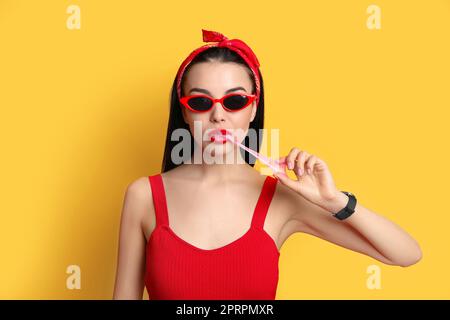 Jeune femme à la mode dans une tenue à épingler mâchant du bubblegum sur fond jaune Banque D'Images