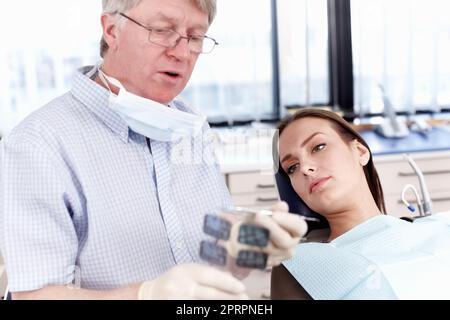 Médecin présentant des rayons X à une patiente. Portrait d'un médecin mature montrant une radiographie dentaire à son patient féminin. Banque D'Images