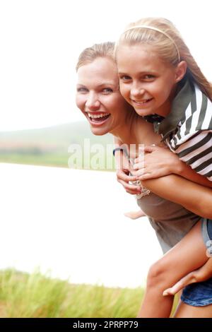 Ma plus grande joie. Riant jeune mère piggysoutenant sa petite fille en plein air - copyspace. Banque D'Images