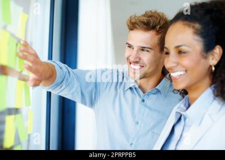 Planification. Homme d'affaires souriant et femme lisant des notes adhésives sur le verre. Banque D'Images