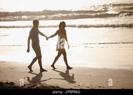 Ils aiment faire de longues promenades sur la plage. Un couple affectueux se promenant sur la plage. Banque D'Images