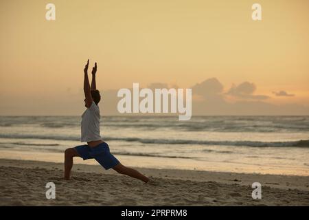 Yoga - la poésie du mouvement. Un homme faisant du yoga sur la plage au coucher du soleil. Banque D'Images