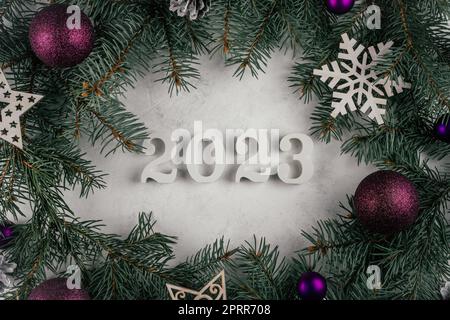 Les numéros 2023 en bois blanc sont posés sur une surface en béton blanc avec des branches d'arbre de Noël, des décorations d'arbre de Noël et des boules violettes. Joyeux Christma Banque D'Images