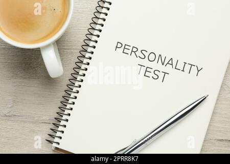 Carnet avec test de personnalité de texte, tasse de café et stylo sur table en bois blanc, pose à plat Banque D'Images