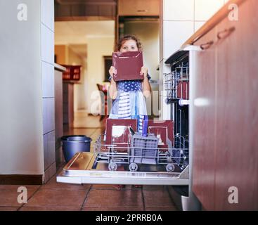 La vaisselle sale entre, la vaisselle propre sort. Portrait d'une adorable petite fille qui charge le lave-vaisselle à la maison Banque D'Images