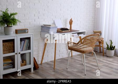 Intérieur confortable du lieu de travail de l'écrivain avec machine à écrire sur le bureau près du mur de briques blanches Banque D'Images