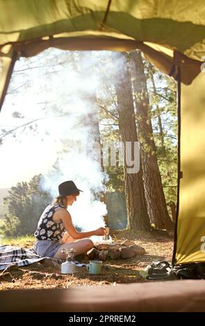 La solitude du feu de camp. Une jeune femme qui fait du café sur un feu ouvert dans un camping Banque D'Images