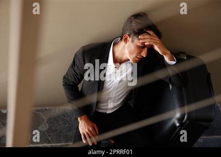 Jetlag... un jeune homme d'affaires épuisé assis sur le sol à côté de ses bagages Banque D'Images