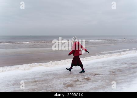 Une femme en rouge marche en hiver le long de la mer Banque D'Images