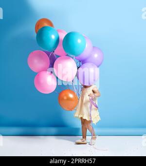 Shes un cutey caché. Une petite fille mignonne debout derrière un tas de ballons. Banque D'Images