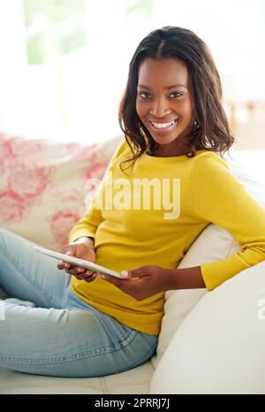 Je n'ai pas besoin de quitter ma maison. Ma tablette a tout ce qu'il vous faut. Portrait d'une jeune femme attrayante utilisant une tablette numérique se détendre à la maison Banque D'Images