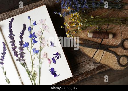 Vieux ciseaux avec de belles fleurs séchées et livre sur table en bois, plat Banque D'Images