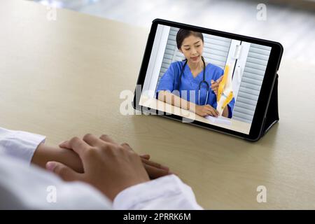 Vue arrière de la femme en robe blanche ont webcam conférence sur ordinateur tablette avec jeune asiatique médecin en uniforme bleu sur l'os, l'articulation, le tendon et le muscle. Banque D'Images