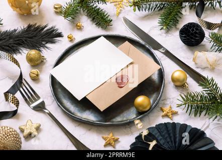 Table de Noël noire et dorée avec une carte, des ornements et des branches de sapin. Maquette Banque D'Images