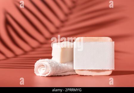 Porte-savon fait à la main avec étiquette vierge et petite serviette sur rose gros plan, feuilles de palmier dures ombres Banque D'Images