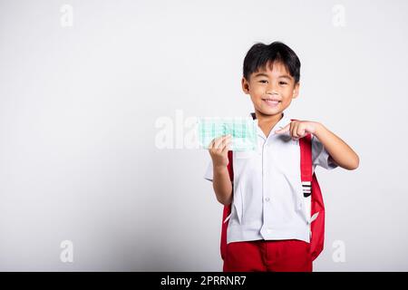 Enfant enfant asiatique étudiant garçon portant l'uniforme thaï étudiant et pointant le doigt pour protéger le masque avant d'aller à l'école Banque D'Images