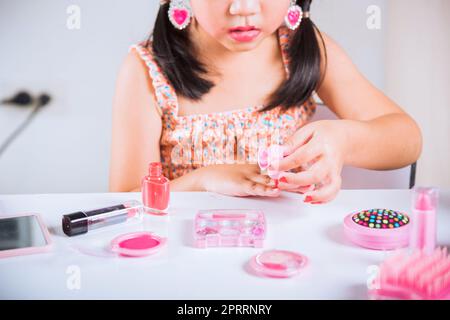 petite fille faisant le maquillage trempette brosse dans la bouteille pour peindre les ongles vernis à ongles rouge elle-même Banque D'Images