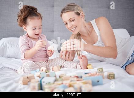 Lit, mère heureuse et bébé avec des jouets jouent avec des blocs de construction de l'éducation de l'alphabet dans la chambre à la maison. L'amour de famille, le développement de l'enfant et le plaisir pour apprendre la petite fille ou l'enfant liant avec la mère Banque D'Images