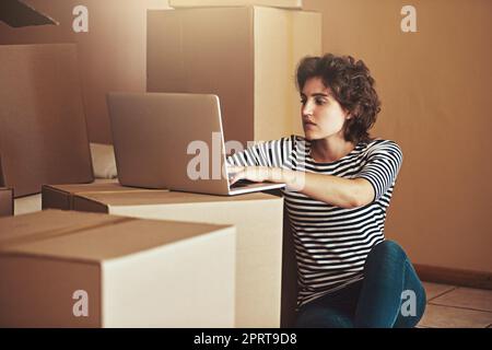 Mise à jour de l'état Nouveau domicile, nouveaux débuts. une jeune femme assise sur le sol et utilisant un ordinateur portable dans sa nouvelle maison Banque D'Images